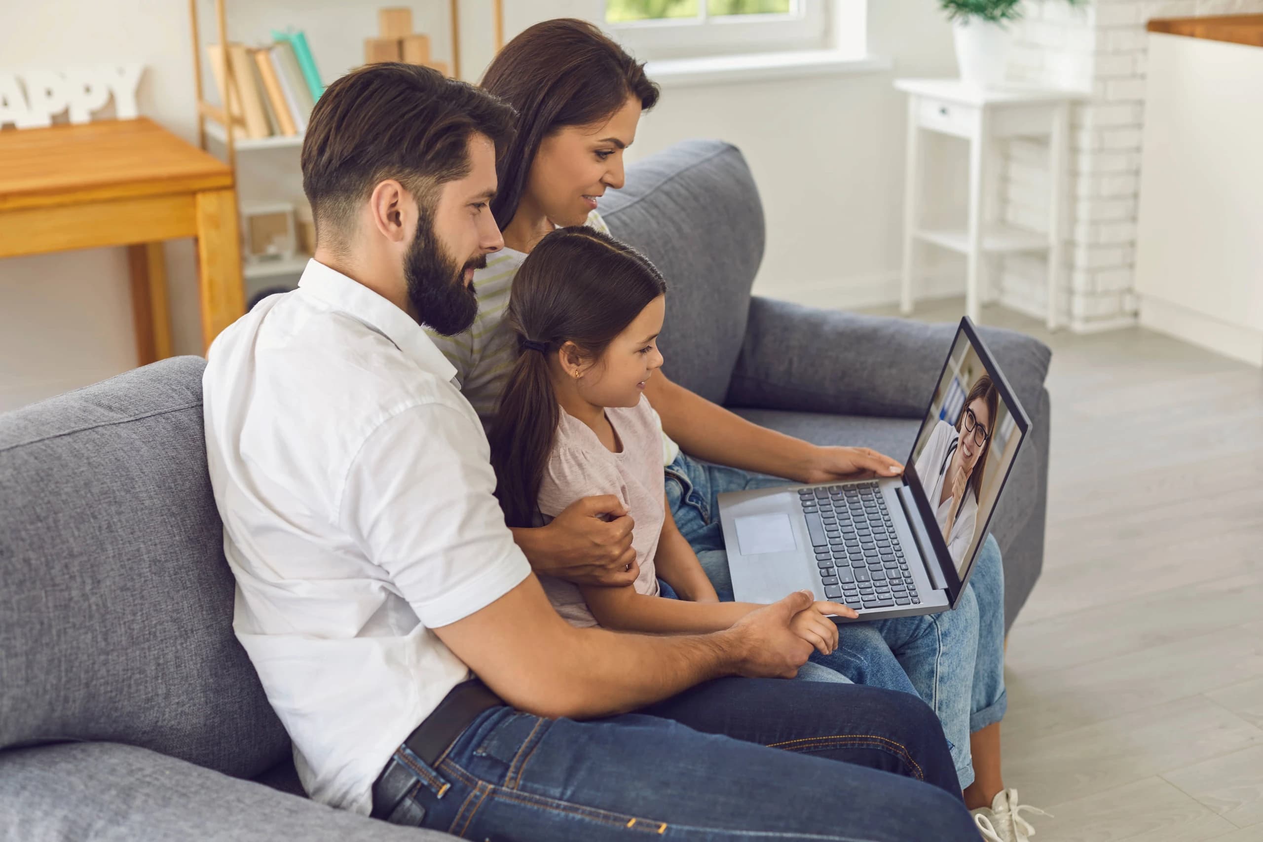 Woman on telehealth video call with doctor while relaxing at home, child visible in background
